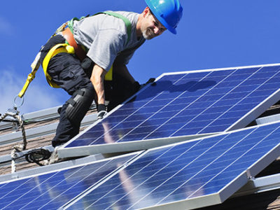 Guy installing solar panels on the top of the roof during a sunny day